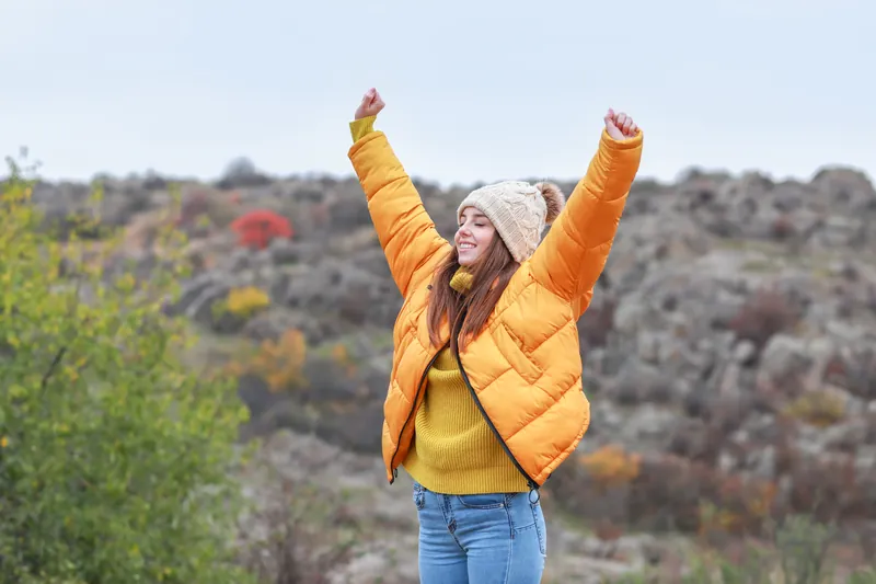 Happy woman in a yellow jacket raising her arms outdoors