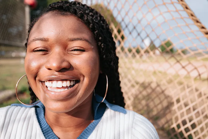 Close-up of a laughing woman with braids and hoop earrings outdoors