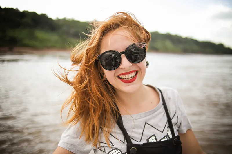 Laughing red-haired woman in sunglasses by a river