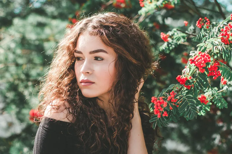 Young woman with curly hair looking aside in a garden with red berries