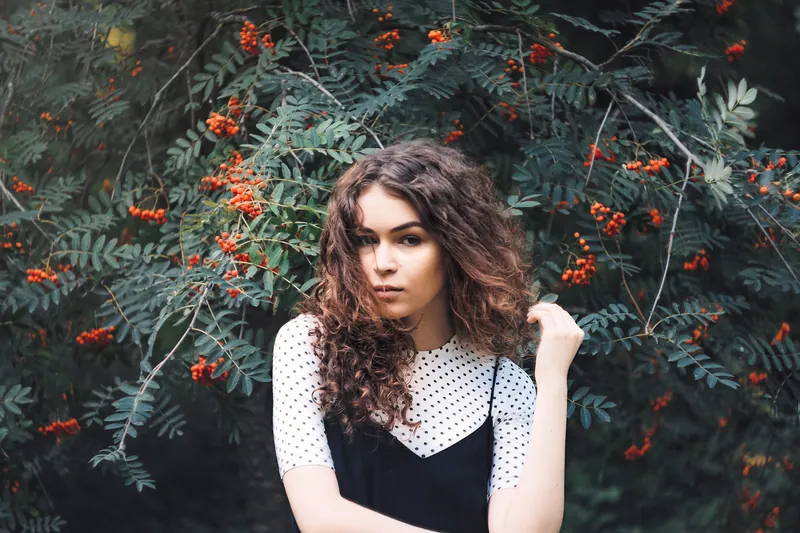 Woman with curly hair in a polka-dot top standing among rowan branches