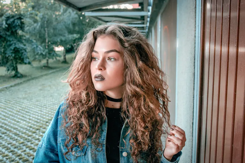 Woman with long wavy hair and a denim jacket on a porch
