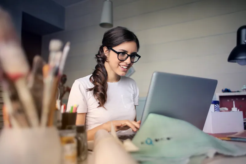 Smiling woman with glasses using a laptop at her desk