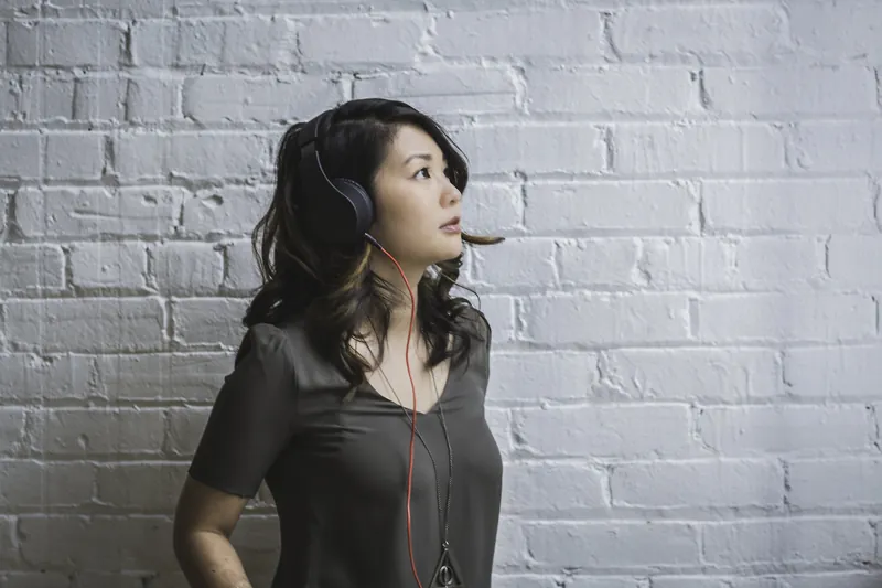 Thoughtful woman with headphones looking up against a white brick wall