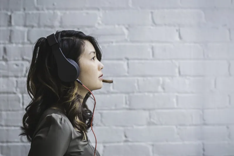 Woman wearing a headset with microphone in front of a white brick wall