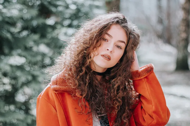 Woman with long curly hair in an orange jacket on a winter day