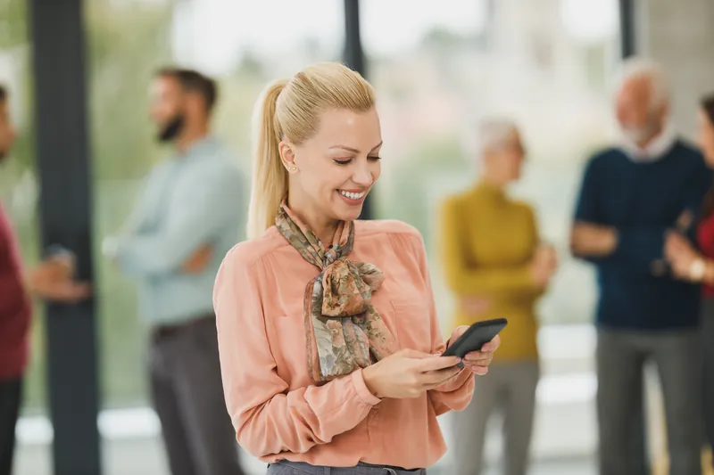 Smiling blonde woman in a peach blouse using her smartphone