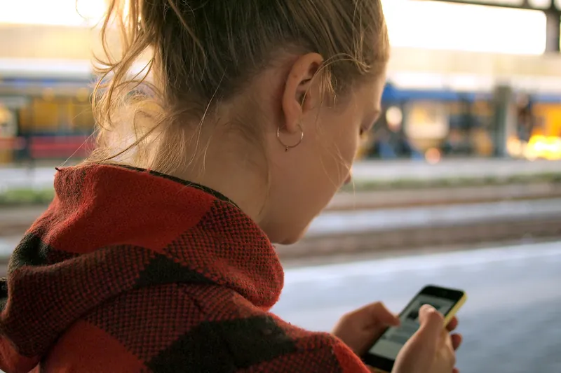 Woman in a red hoodie checking her phone at a train station