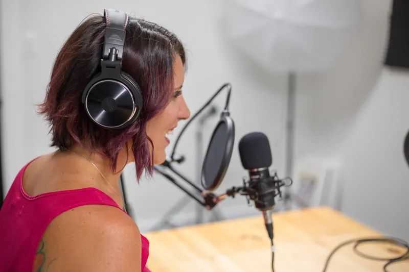 Smiling woman with headphones talking into a studio microphone