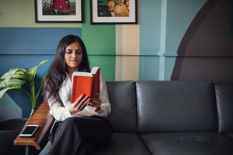 Woman reading a red book on a leather sofa