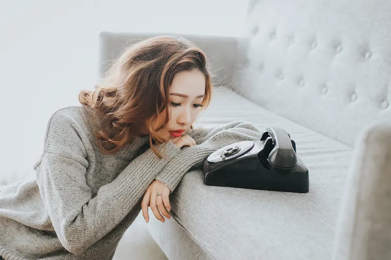 Woman resting her head on a sofa next to a vintage telephone