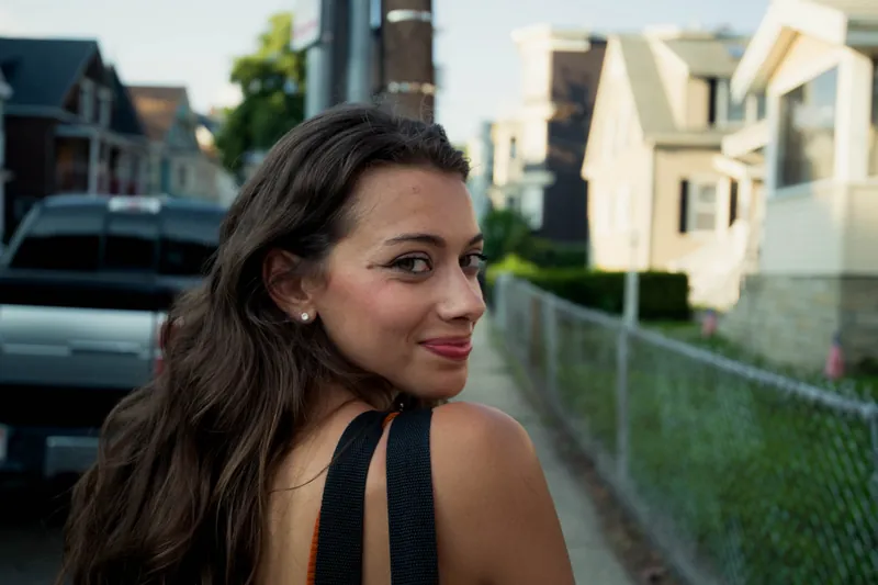 Woman with long dark hair smiling over her shoulder on a street