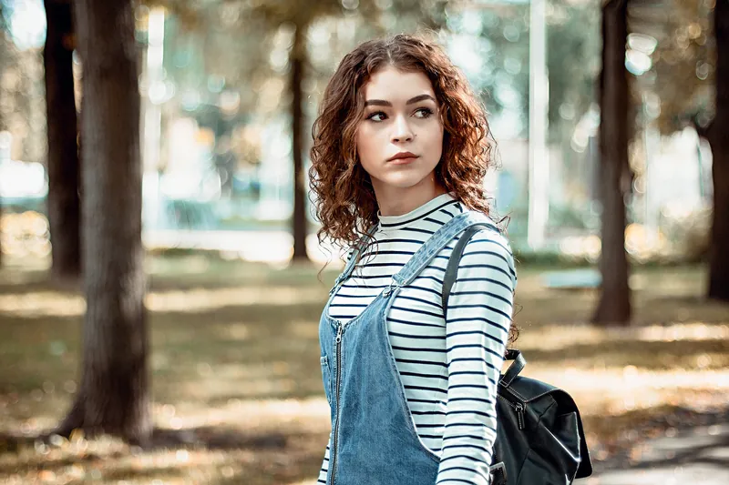 Woman with a striped top, denim overalls and a backpack in a sunny park