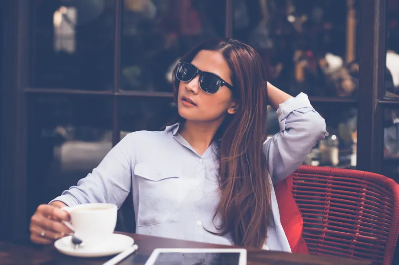 Woman in sunglasses enjoying a coffee at a café table with a tablet