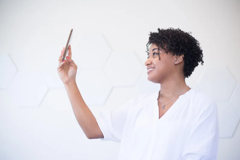 Smiling woman with curly hair taking a selfie with her phone