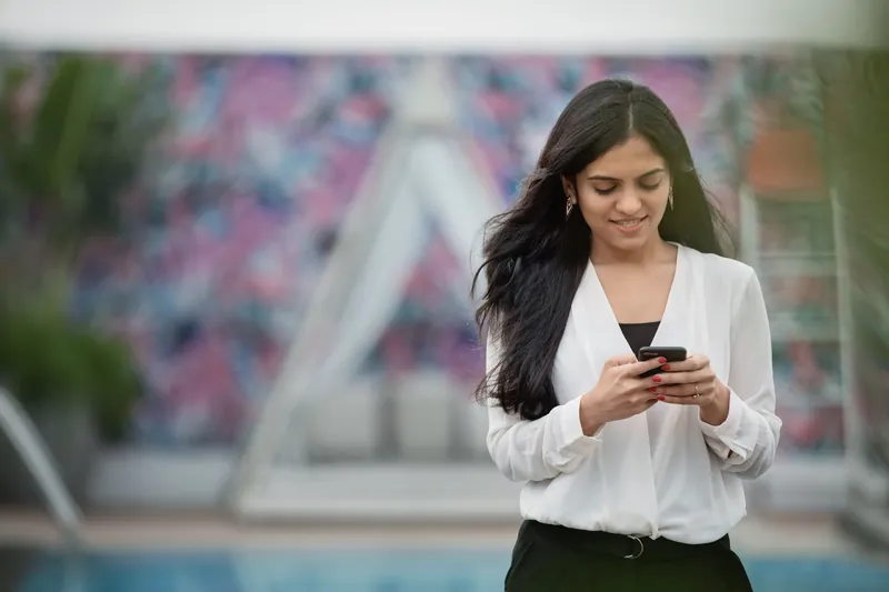 Woman in a white blouse smiling at a message on her phone